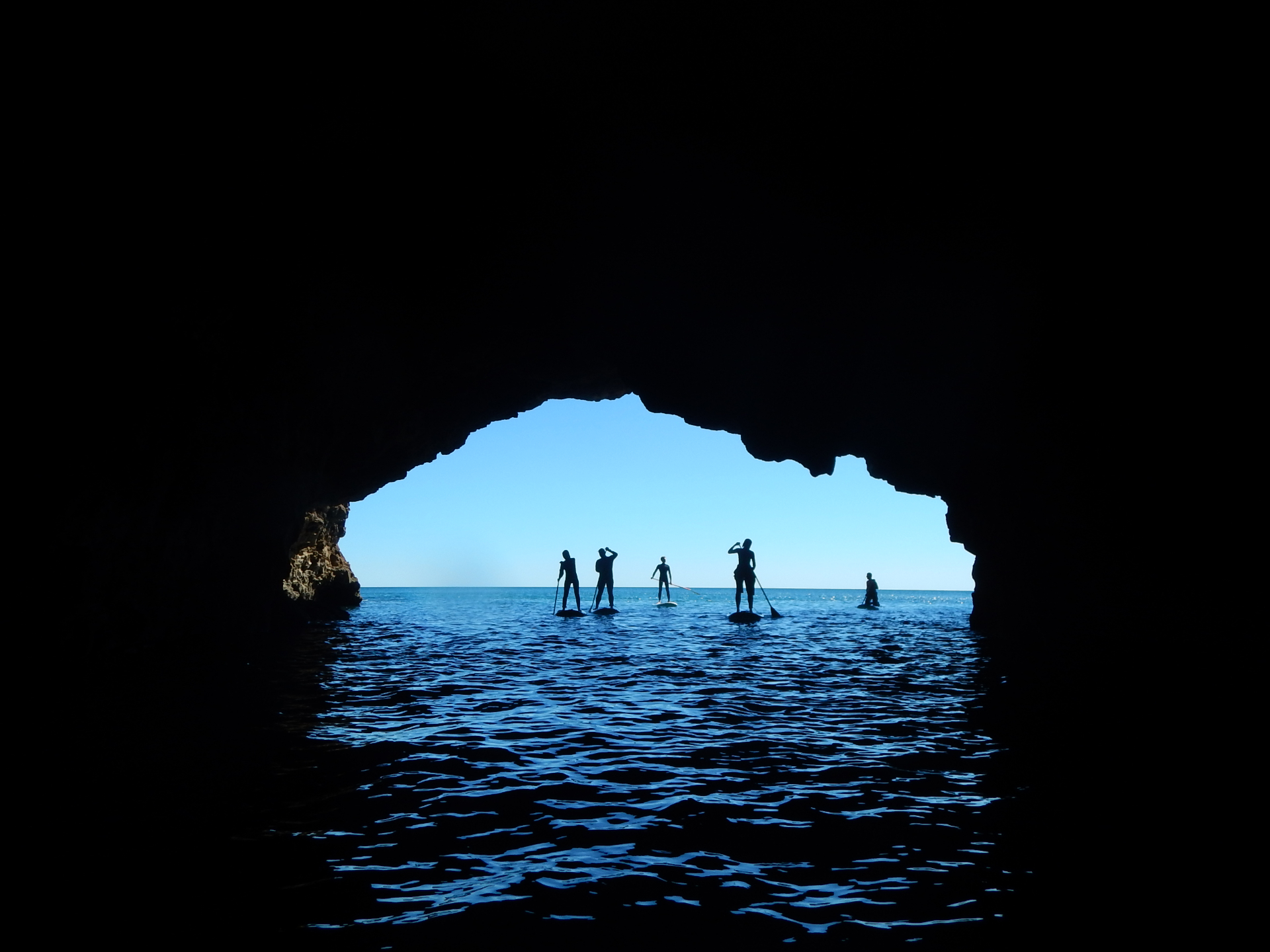 Stand Up Paddlers silhouetted inside a golden Algarve sea cave at sunrise